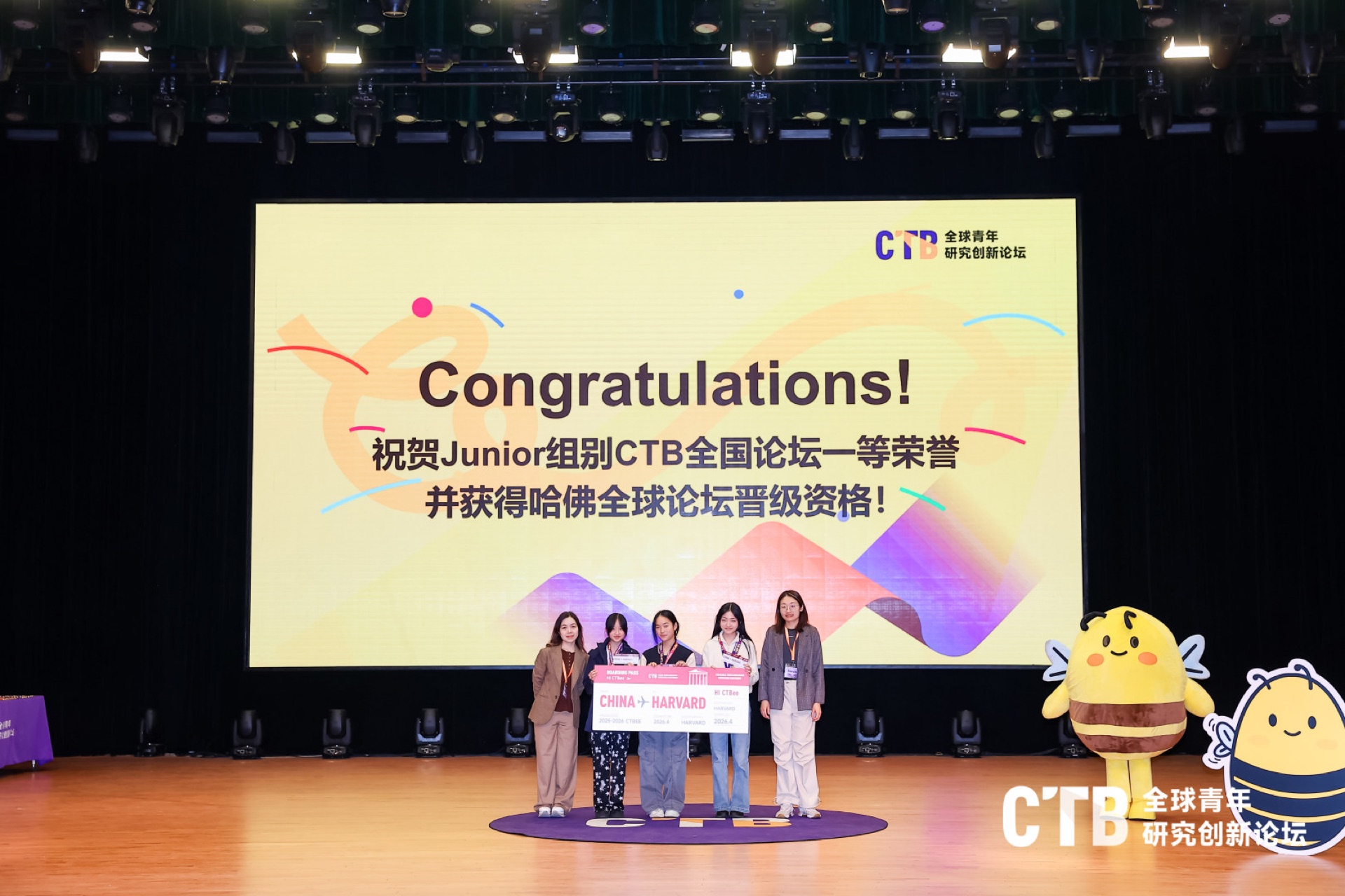 Empact 三位学员与教练在 CTB 全国论坛颁奖台合影，屏幕显示 Junior 组别一等奖与哈佛全球论坛晋级资格